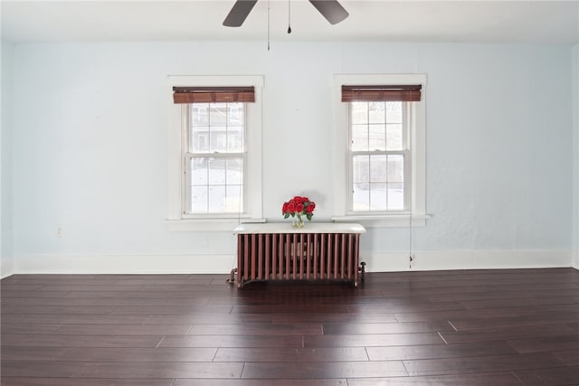 empty room featuring radiator heating unit, dark wood finished floors, a ceiling fan, and baseboards