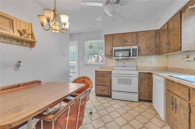 kitchen with white appliances, pendant lighting, sink, and ceiling fan with notable chandelier