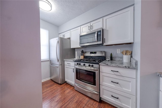 kitchen with appliances with stainless steel finishes, a textured ceiling, light stone countertops, white cabinets, and dark hardwood / wood-style floors