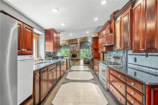 kitchen with appliances with stainless steel finishes, tasteful backsplash, dark stone counters, lofted ceiling, and sink