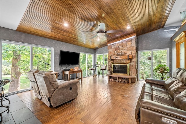 living room with a stone fireplace, lofted ceiling, ceiling fan, light hardwood / wood-style floors, and wood ceiling