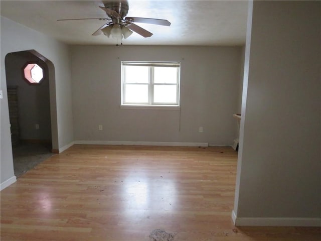 empty room featuring arched walkways, baseboards, a ceiling fan, and light wood-style floors