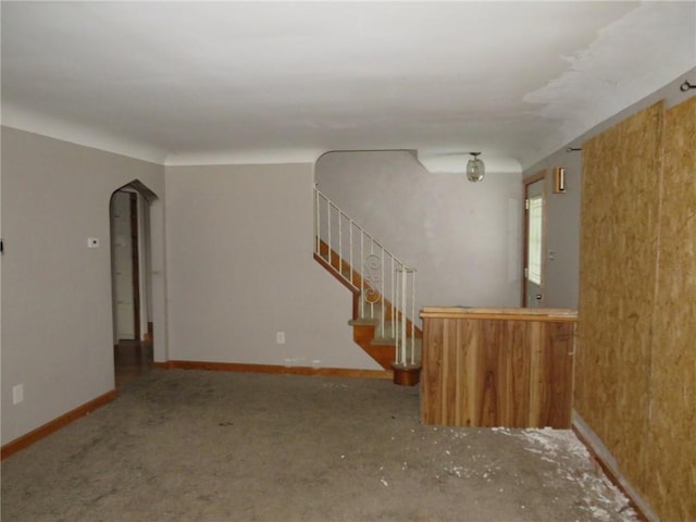 unfurnished living room with arched walkways, stairway, and baseboards