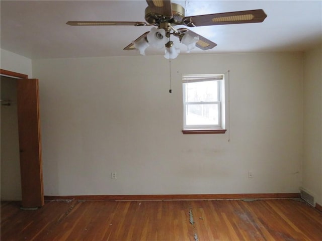 empty room featuring a ceiling fan, dark wood-style flooring, visible vents, and baseboards