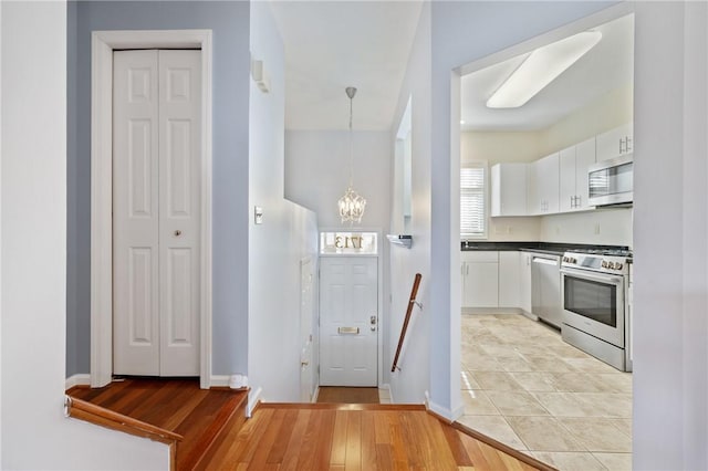 kitchen with white cabinets, pendant lighting, stainless steel appliances, and light hardwood / wood-style flooring