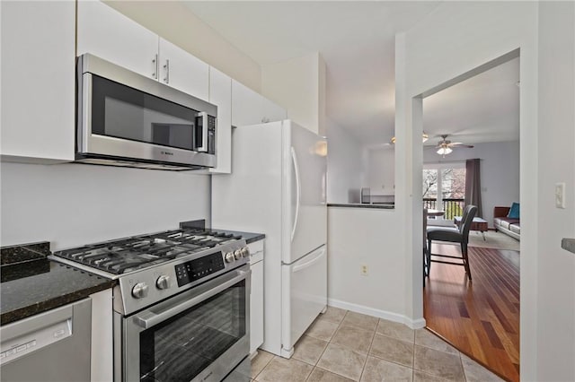 kitchen with stainless steel appliances, dark stone counters, ceiling fan, light tile patterned flooring, and white cabinetry