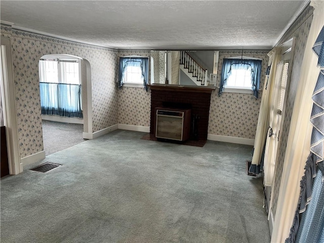 unfurnished living room featuring a healthy amount of sunlight, wallpapered walls, carpet flooring, and a textured ceiling
