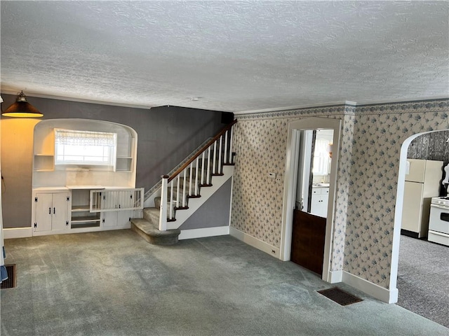 unfurnished living room with stairway, a textured ceiling, wallpapered walls, carpet floors, and visible vents