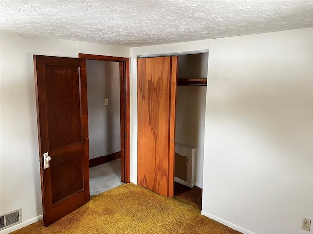 unfurnished bedroom with carpet floors, a textured ceiling, a closet, and visible vents