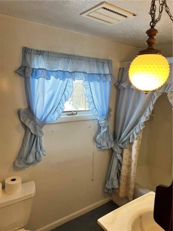 bathroom featuring baseboards, a textured ceiling, visible vents, and toilet