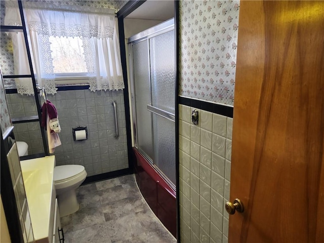 full bathroom with tile walls, enclosed tub / shower combo, vanity, and toilet