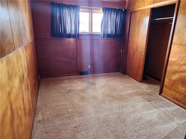 unfurnished bedroom with carpet, a closet, and wooden walls