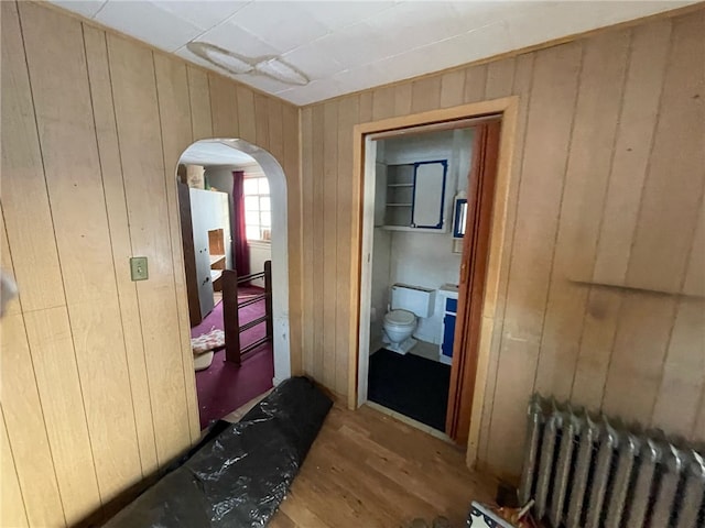 corridor featuring light hardwood / wood-style floors, wood walls, and radiator heating unit