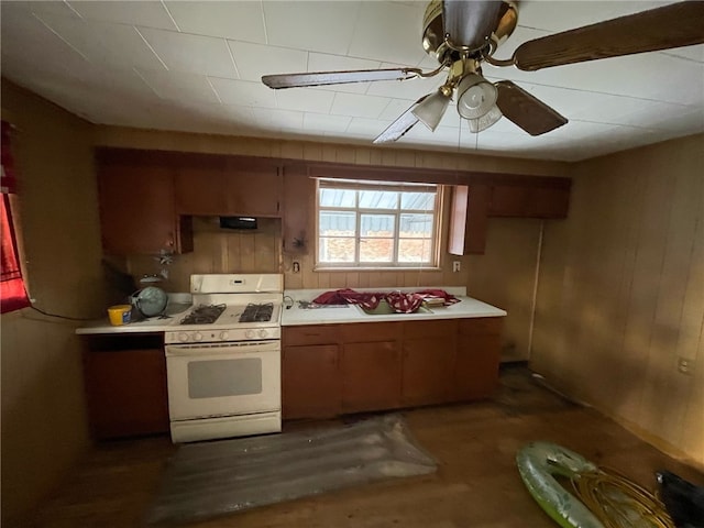 kitchen with white gas range, ceiling fan, and wooden walls