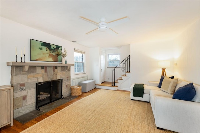 living room featuring ceiling fan, radiator, hardwood / wood-style floors, and a stone fireplace