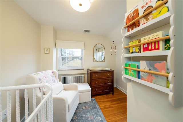 bedroom with radiator heating unit, a nursery area, and hardwood / wood-style floors