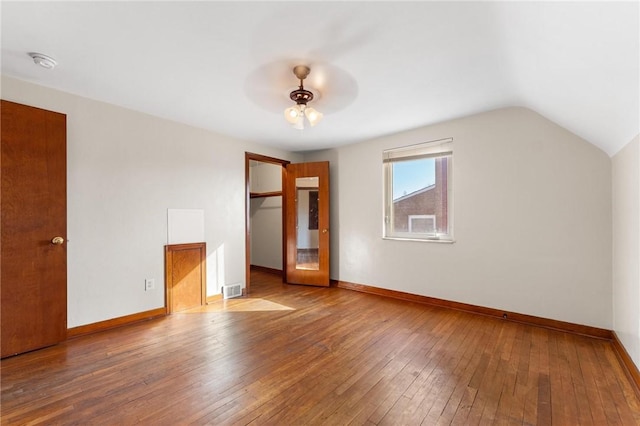 unfurnished bedroom featuring a walk in closet, lofted ceiling, wood-type flooring, and a closet