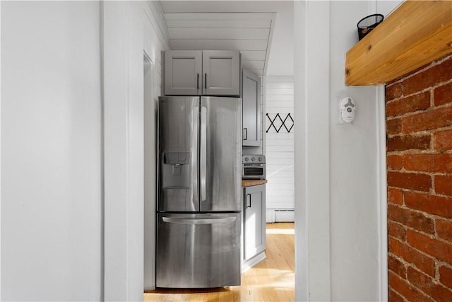 kitchen with stainless steel refrigerator with ice dispenser, wooden counters, brick wall, a baseboard radiator, and gray cabinets