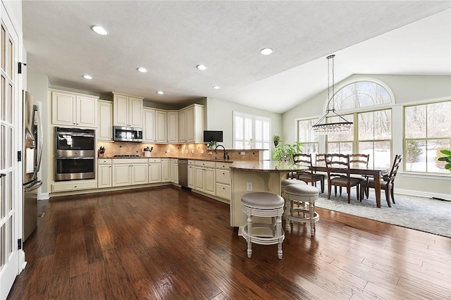 kitchen with a breakfast bar, cream cabinetry, decorative light fixtures, appliances with stainless steel finishes, and a peninsula