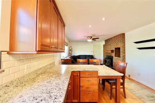 1219 Minnesota Ave, Natrona Hts/Harrison Twp, PA 15065 - kitchen with a ceiling fan, light stone counters, brown cabinetry, backsplash, and a peninsula