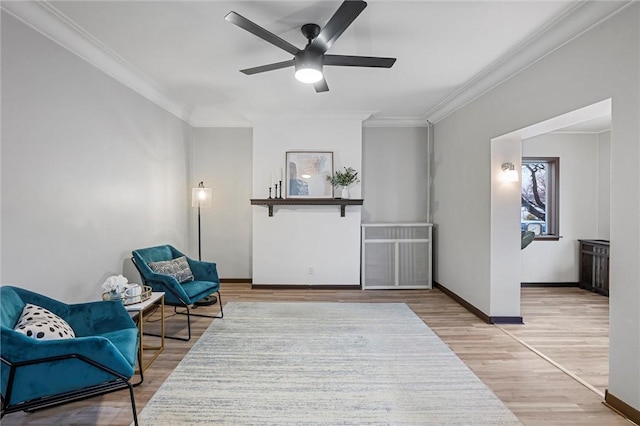 living area featuring a ceiling fan, crown molding, baseboards, and wood finished floors