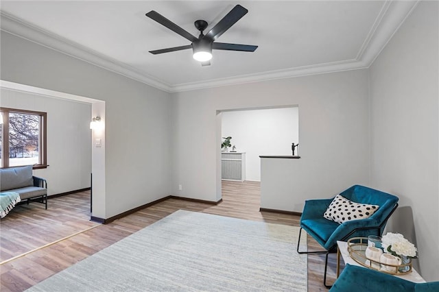 living area with a ceiling fan, baseboards, ornamental molding, and wood finished floors