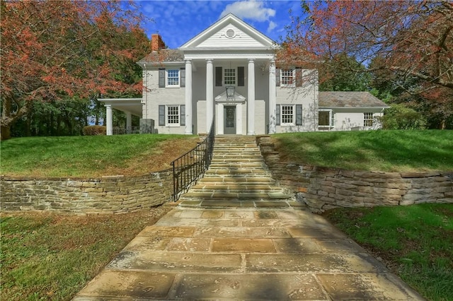 neoclassical home featuring a chimney, a front lawn, and stucco siding