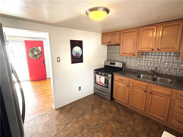 kitchen featuring appliances with stainless steel finishes, dark countertops, brown cabinetry, and a sink