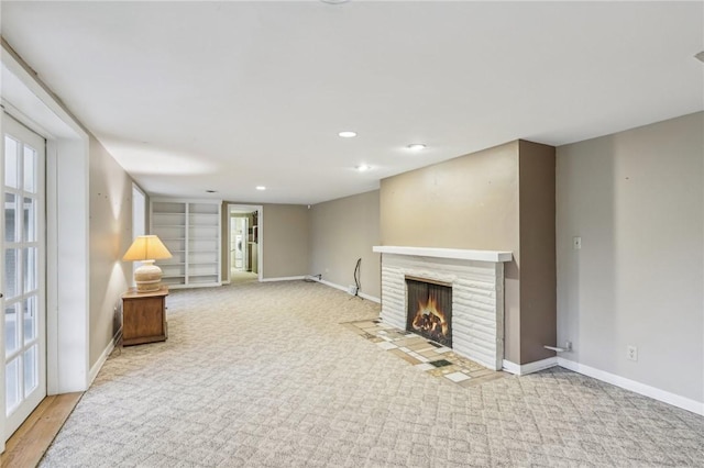 unfurnished living room with recessed lighting, a fireplace with flush hearth, baseboards, and light colored carpet