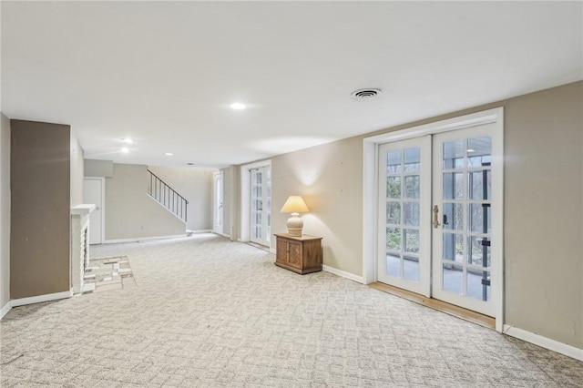 interior space featuring baseboards, visible vents, a fireplace with raised hearth, stairway, and french doors