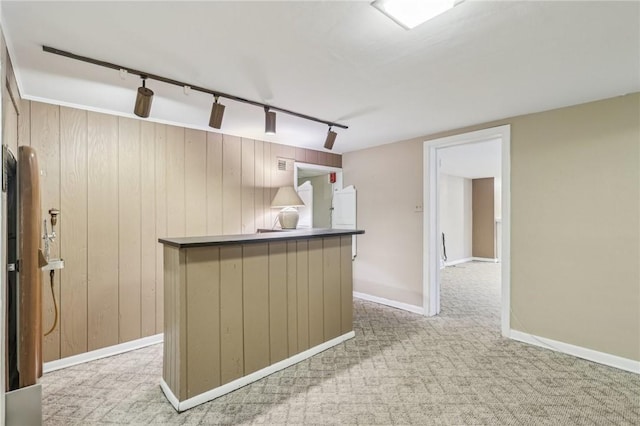 kitchen featuring dark countertops, light carpet, wood walls, track lighting, and baseboards