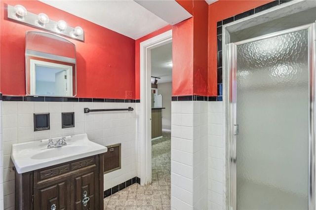 bathroom with a stall shower, wainscoting, tile walls, and vanity