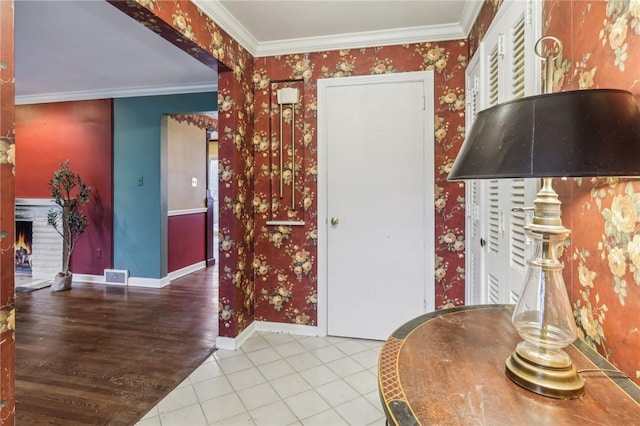 tiled entryway with a warm lit fireplace, ornamental molding, baseboards, and wallpapered walls