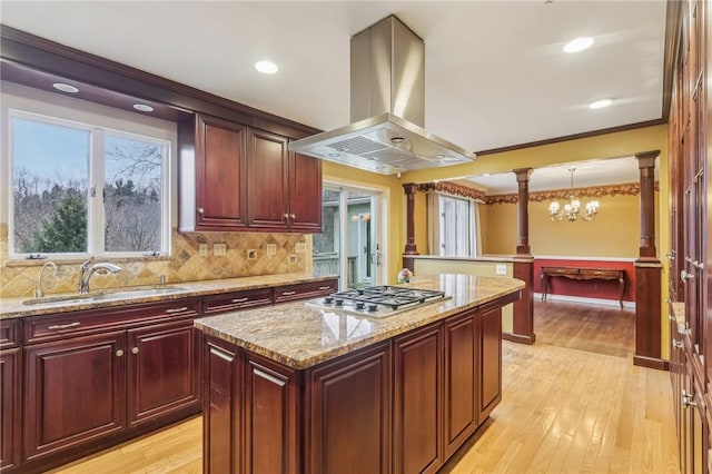 kitchen with decorative columns, a center island, hanging light fixtures, island exhaust hood, and a sink