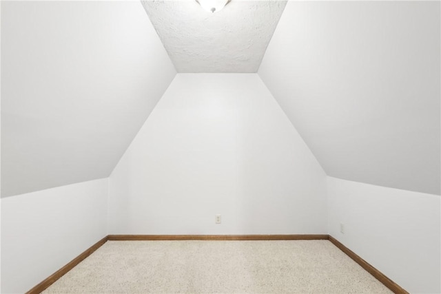 additional living space featuring carpet, vaulted ceiling, and a textured ceiling