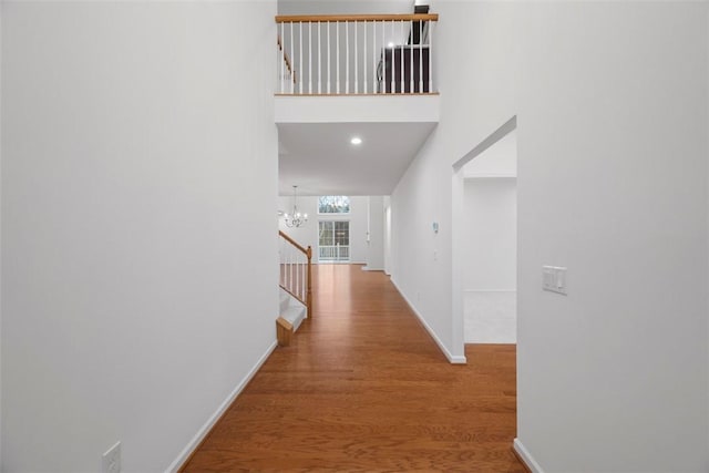 corridor with baseboards, stairway, wood finished floors, a high ceiling, and a notable chandelier