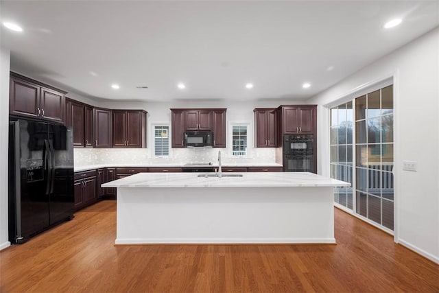 kitchen featuring a sink, light wood-style floors, light countertops, black appliances, and a center island with sink