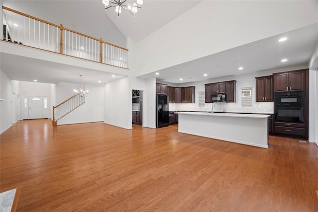 unfurnished living room with a towering ceiling, wood finished floors, a notable chandelier, a sink, and recessed lighting