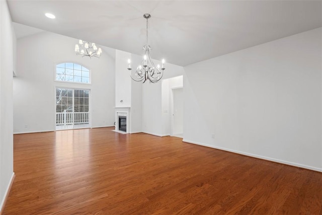 unfurnished living room featuring an inviting chandelier, a fireplace with flush hearth, wood finished floors, high vaulted ceiling, and baseboards