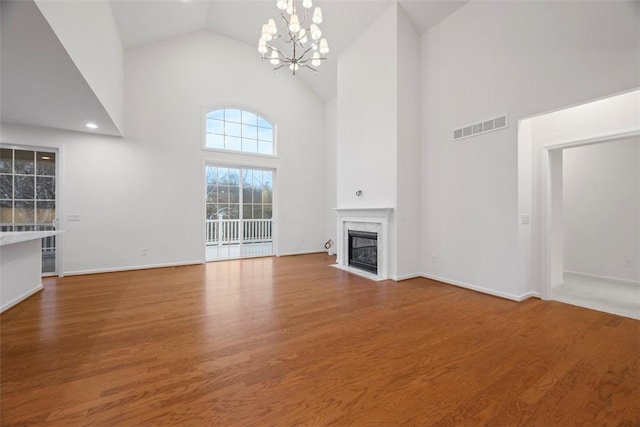 unfurnished living room with visible vents, wood finished floors, high vaulted ceiling, a notable chandelier, and a high end fireplace