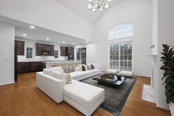 living room with a chandelier, high vaulted ceiling, baseboards, and wood finished floors