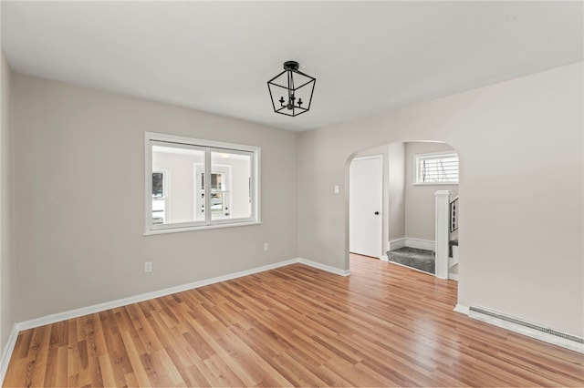 spare room featuring light wood-type flooring, a notable chandelier, and baseboard heating