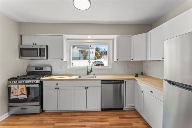 kitchen featuring stainless steel appliances, butcher block counters, sink, tasteful backsplash, and white cabinets