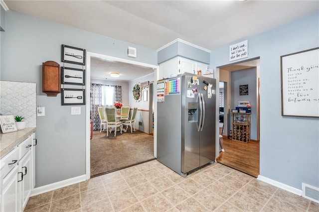 kitchen featuring white cabinets, stainless steel fridge, and light colored carpet