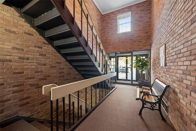 hall featuring brick wall, carpet flooring, and a high ceiling