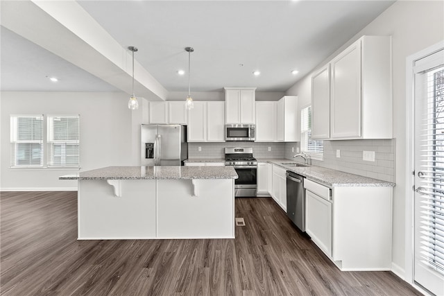 kitchen with sink, light stone counters, a center island, white cabinetry, and stainless steel appliances