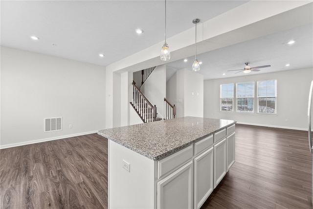 kitchen with light stone countertops, white cabinets, decorative light fixtures, a kitchen island, and dark hardwood / wood-style floors