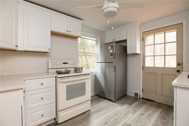 kitchen featuring white electric range, stainless steel refrigerator, white cabinetry, and a wealth of natural light