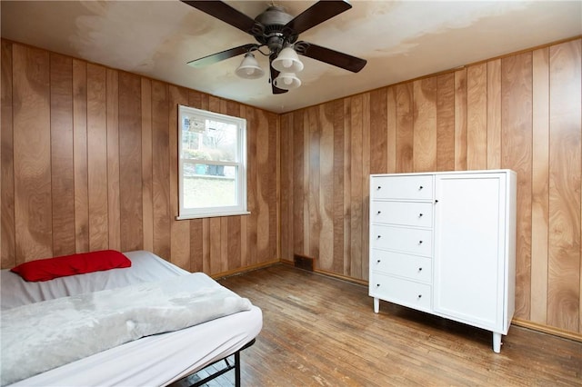 bedroom featuring wooden walls, ceiling fan, and light hardwood / wood-style flooring