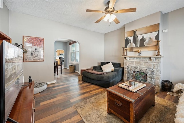 living area featuring a fireplace, a textured ceiling, baseboards, arched walkways, and dark wood-style floors